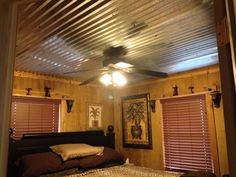 a bed sitting under a ceiling fan in a bedroom next to two windows with blinds on them