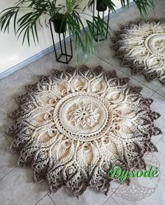 two crocheted rugs sitting on the floor next to a potted plant