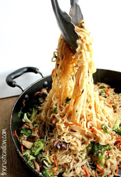 someone is lifting noodles from a pan with broccoli and carrots on it