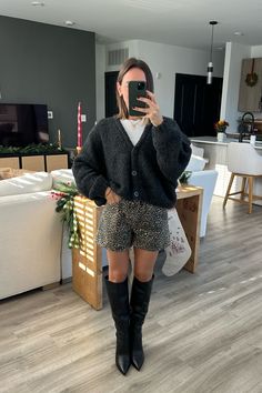 a woman taking a selfie in her living room wearing leopard print shorts and knee high boots