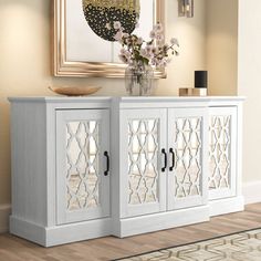 a white sideboard with mirrored doors and flowers in a vase next to a mirror