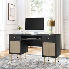 a desk with a computer on it in front of a window and a rug underneath