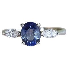 This stunning blue sapphire engagement ring features a 1ct oval-shaped blue origin natural sapphire as the centerpiece, surrounded by sparkling white zircon gemstones on both sides. The combination of the blue sapphire and white zircon stones creates an elegant and timeless look that is perfect for any occasion. The sapphire is of high quality and origin, giving it a rich and vivid blue color. The zircon gemstones add an extra layer of sparkle and brilliance to this already stunning ring. The Pl Oval Blue Three-stone Diamond Ring, Oval Blue Multi-stone Sapphire Ring, Heirloom Oval Sapphire Three-stone Ring, Oval Three-stone Sapphire Ring With Cubic Zirconia, Luxury Multi-stone Oval Sapphire Ring, 3 Stone Ring, Blue Origin, Blue Sapphire Engagement Ring, 3 Stone Rings