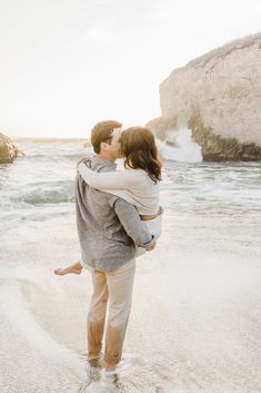 a man and woman standing on the beach kissing while holding each other's arms