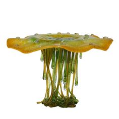 a green and yellow glass sculpture with water droplets on it's bottom, in front of a white background