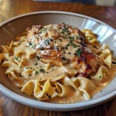 a white bowl filled with pasta and meat covered in gravy on top of a wooden table