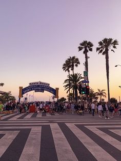 people are crossing the street in front of palm trees and an arch that says welcome to los angeles