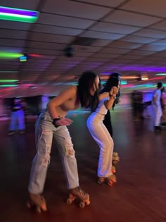 two women on roller skates in an indoor area with lights and people walking around