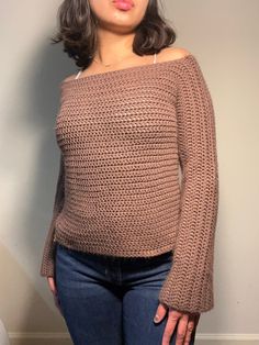 a woman standing in front of a wall with her hands on her hips wearing a brown sweater