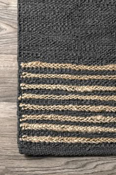 a black rug with brown and tan stripes on top of wooden flooring next to a gray wall