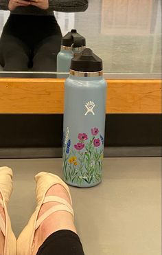 a woman sitting on the ground with her feet up next to a water bottle that has flowers painted on it