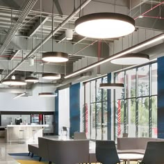 an office with chairs and tables in front of large windows, lights hanging from the ceiling