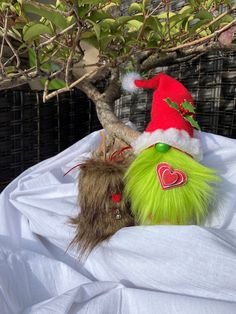 a green stuffed animal with a santa hat on top of it's head next to a tree