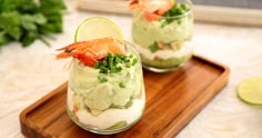 two glasses filled with food and garnished with limes on a wooden tray