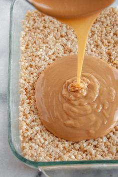 peanut butter being poured into a glass dish with oatmeal in the background