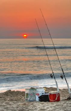 two fishing rods on the beach at sunset with an outboard boat in the background