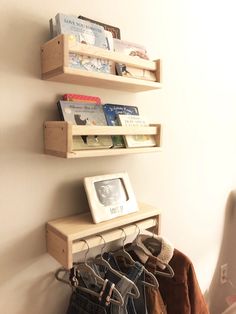 two wooden shelves holding books and clothes hang on the wall next to a coat rack