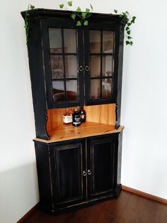 a black china cabinet with glass doors and wooden shelves on the top, in a room with hardwood floors