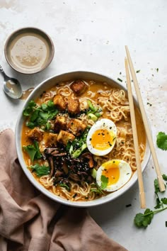 an overhead view of a bowl of ramen with noodles, eggs and greens on the side