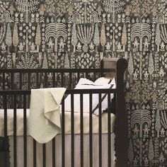 a baby's crib with a blanket on top of it and wall paper in the background