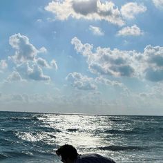 a man sitting on top of a beach next to the ocean under a cloudy blue sky