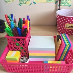 a pink basket filled with lots of different colored pens and markers on top of a wooden table