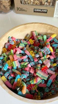 a wooden bowl filled with lots of colorful gummy bears next to a box of krispy kreme cereal