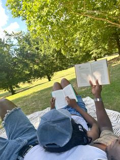 two people laying on a blanket reading books in the park with their feet up against each other