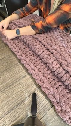 a woman is sitting on the floor with a large knitted blanket in front of her