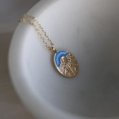 Light up your style with our Gold Filled Crescent Moon & Stars Oval Charm Necklace, a celestial-inspired piece that brings the magic of the night sky into your everyday wardrobe. This enchanting necklace features an oval-shaped charm with a serene blue background, adorned with a delicate crescent moon at its center. The moon is surrounded by bursts of light leading to tiny stars, all accented with sparkling cubic zirconia stones that add a touch of brilliance to the design.  This celestial neckl Blue Celestial Necklaces With Sun And Moon Design, Blue Sun And Moon Pendant Necklace, Blue Necklace With Sun And Moon Design For Gift, Blue Sun And Moon Necklace For Gift, Blue Sun And Moon Design Necklace For Gift, Blue Celestial Necklace With Moon Charm, Celestial Pendant, Celestial Necklace, Tiny Star