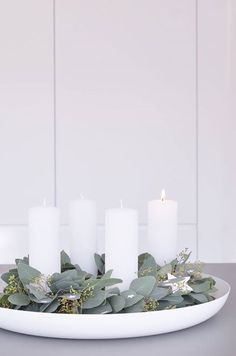 white candles and greenery are arranged on a plate