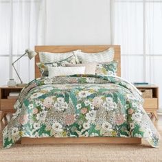 a bed in a room with white curtains and green floral comforter set on top of it