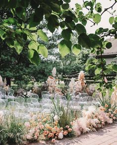 an outdoor ceremony with clear chairs and flowers in the foreground, surrounded by greenery