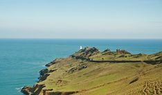 an aerial view of the ocean and grassy hills with a light house on top in the distance