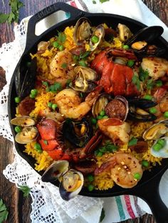 a skillet filled with seafood and rice on top of a table next to utensils