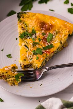 a slice of quiche on a white plate with a fork and parsley garnish