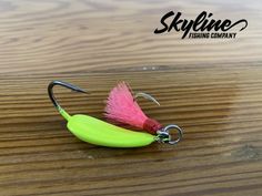 a pink and green fishing lure on a wooden table with the name sklfine fishing company