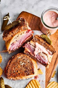 two sandwiches cut in half on a cutting board with pickles and chips next to it