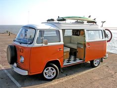 an orange and white vw bus parked on top of a beach next to the ocean