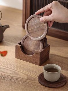 a person holding a wooden coaster in front of a cup and saucer on a table