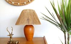 a wooden table topped with a lamp next to a green plant and a brown vase