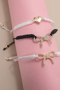 three bracelets with bows on them are sitting on a pink napkin holder and one has a gold bow