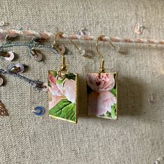 two square earrings with pink flowers on them sitting on top of a piece of fabric