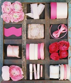 pink and white items are arranged in an old wooden box, including ribbons, laces, flowers, and more