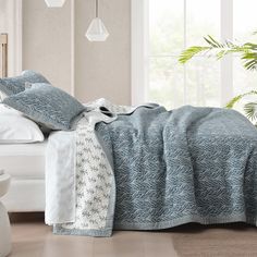 a bed with blue and white comforter next to a potted plant on the floor