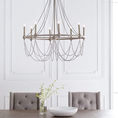 a chandelier hanging from the ceiling in a white dining room with gray chairs