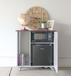 an old fashioned microwave sits on top of a small cabinet with a clock above it