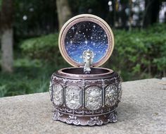 an ornate metal box with a clock in it's center on top of a rock