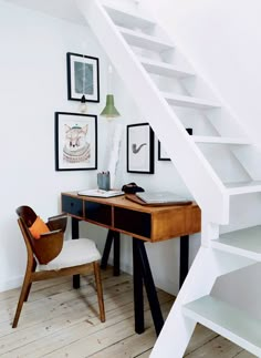 a desk and chair under a stair case in a room with pictures on the wall