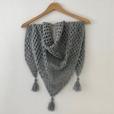 a crocheted shawl hanging on a wooden hanger with tassels